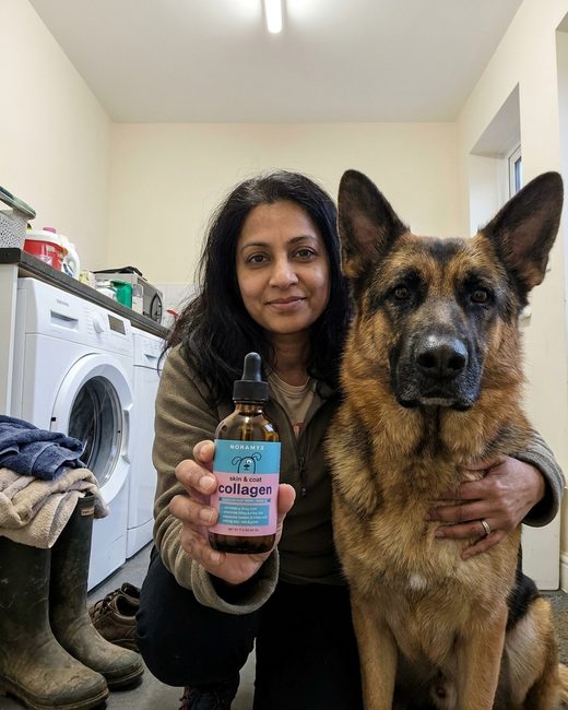A woman crouched beside a German Shepherd in a utility room, holding the Noramyx bottle toward the camera.
