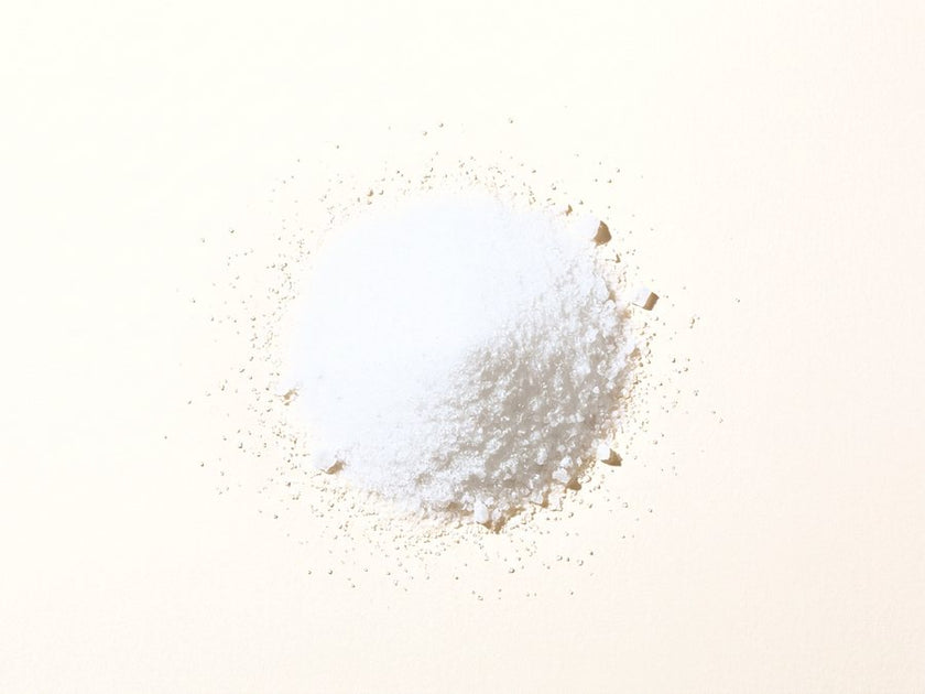 A small pile of white crystalline vitamin C powder on a warm cream surface.