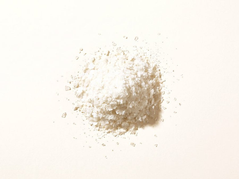 A small pile of translucent flaky hyaluronic acid powder on a warm cream surface.